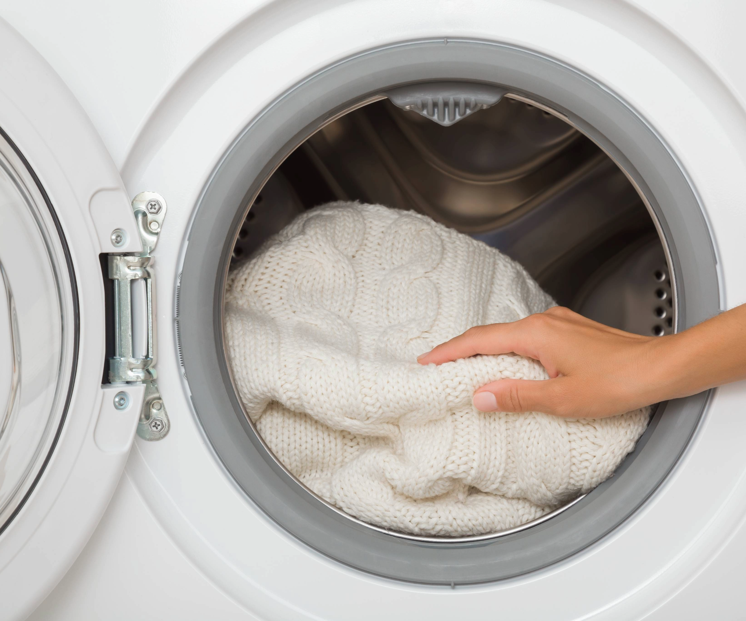 Hand touching white knit in tumble dryer