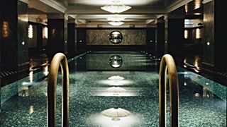 Brass swimming-pool steps leading into a dark tiled swimming pool, with chandeliers above
