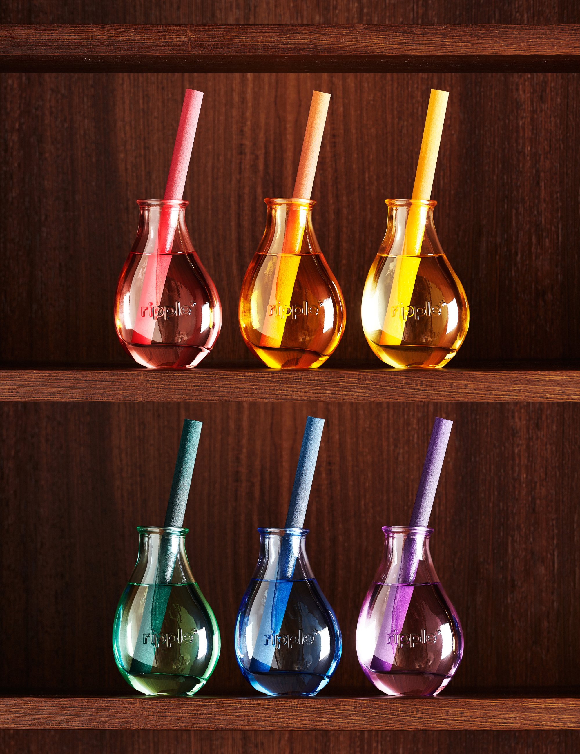 Set of six ripple+ Home reed diffuers in a rainbow of colorways, pictured sitting on a warm wooden shelf