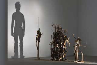 A closer view of one shadow sculpture made out of junk, metal, and wood. The light shines on the sculpture and casts a shadow on the wall. The shadow portrays a man.