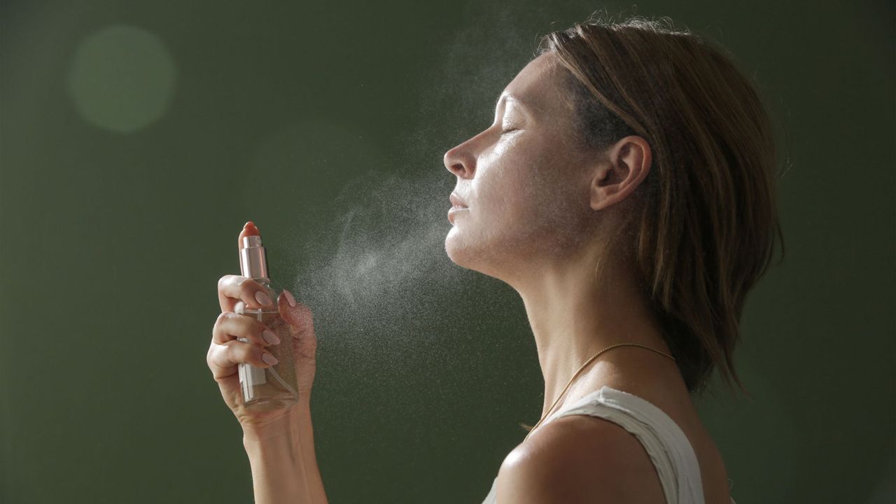 best face mists - image of a woman spraying a mist onto her face side on - gettyimages 1414252650