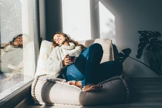 A woman relaxing by a window draped in sun light.