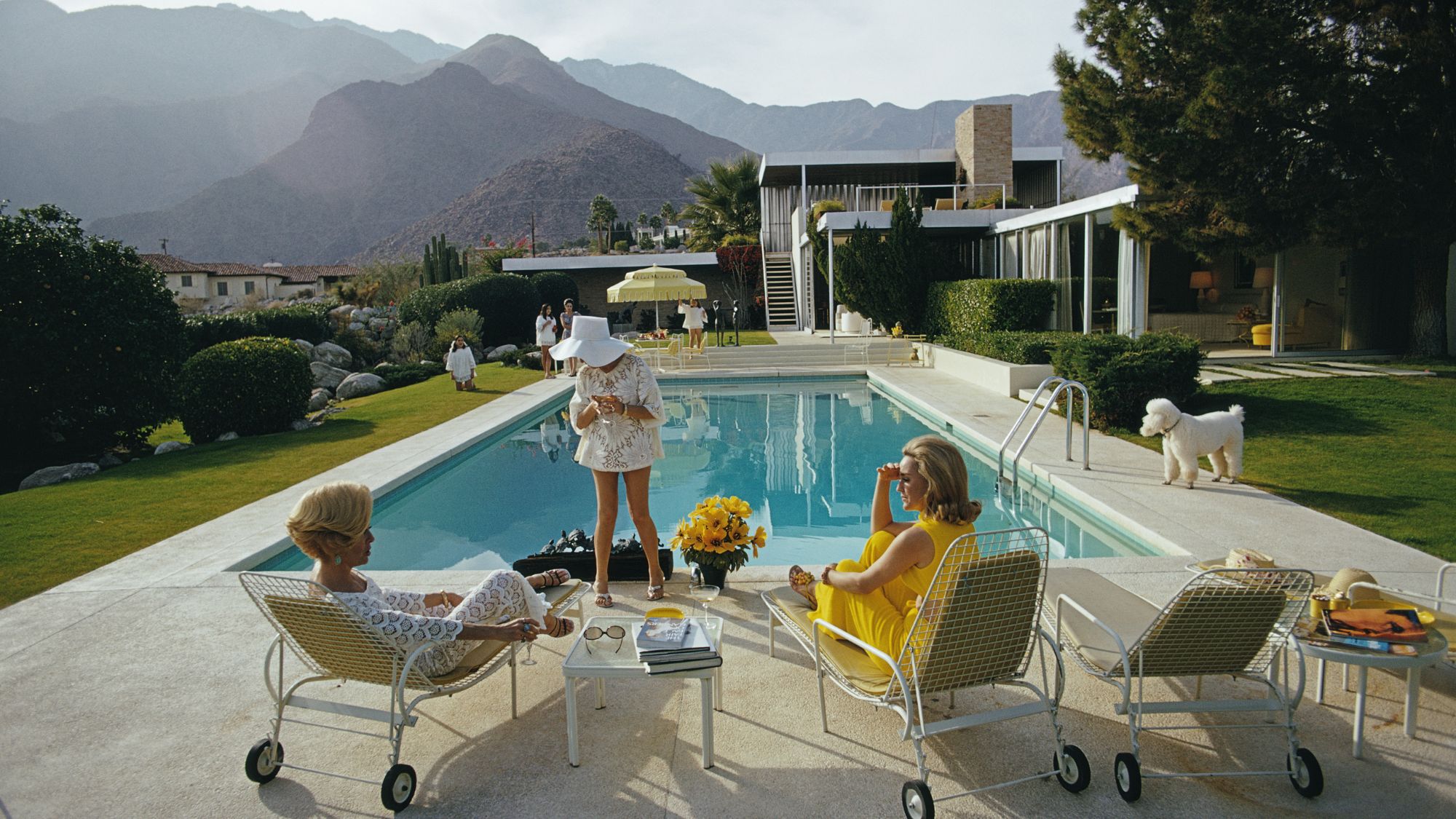 Former fashion model Helen Dzo Dzo Kaptur (in white lace), Nelda Linsk (in yellow), wife of art dealer Joseph Linsk, and actress Lita Baron (in white sunhat) at the Kaufmann Desert House in Palm Springs, California, January 1970. The Linsks are the current owners of the house. (Photo by Slim Aarons/Getty Images)