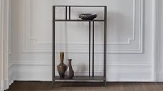 Close-up image of a white wall with molding that has a chic, black console table with two ceramic vases and a ceramic dish on it.