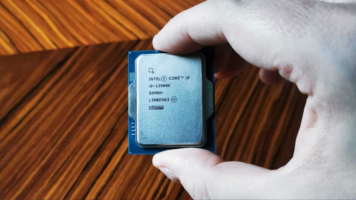 Hand holding Intel Core i9-13900K CPU in front of woodgrain table