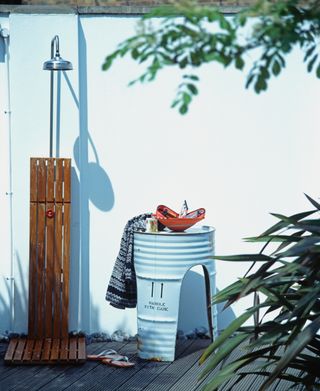 outdoor shower against a white wall with a rustic wooden platform