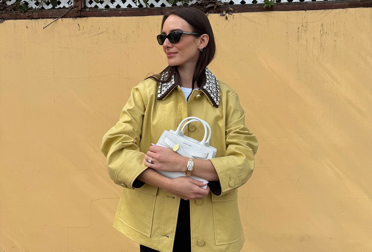 Woman wearing a yellow Veronica Beard coat and holding a white handbag.