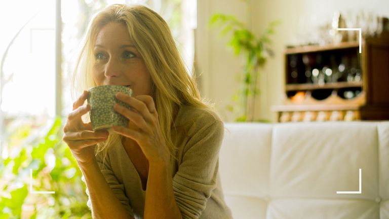 Woman sitting on sofa drinking cup of herbal tea with plants in the background