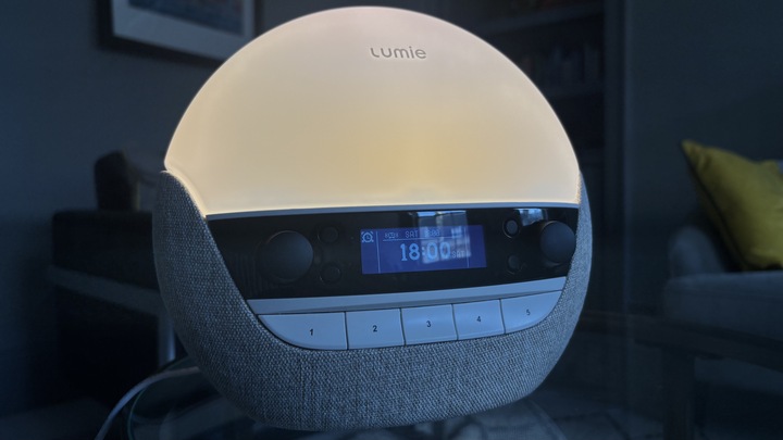 The Lumie Bodyclock Luxe 700FM sunrise alarm clock lighting a dark room with a sunrise-mimicking glow.