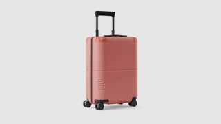 A pink July travel suitcase on a beige background.