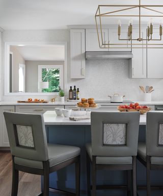 Kitchen with blue island, bar stools, pendant light and gray cabinets beyond