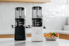 a lifestyle image of one black and one white model of the Nama J2 Juicer, sitting on a countertop 