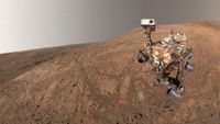 A rover sits on the reddish brownish surface of Mars