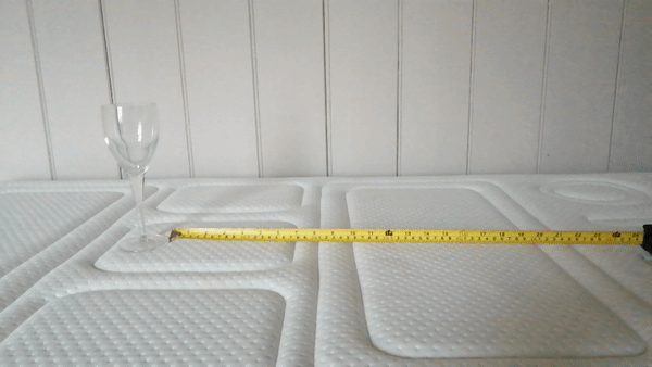 Weight dropping on surface of Otty Pure mattress, next to an empty wine glass