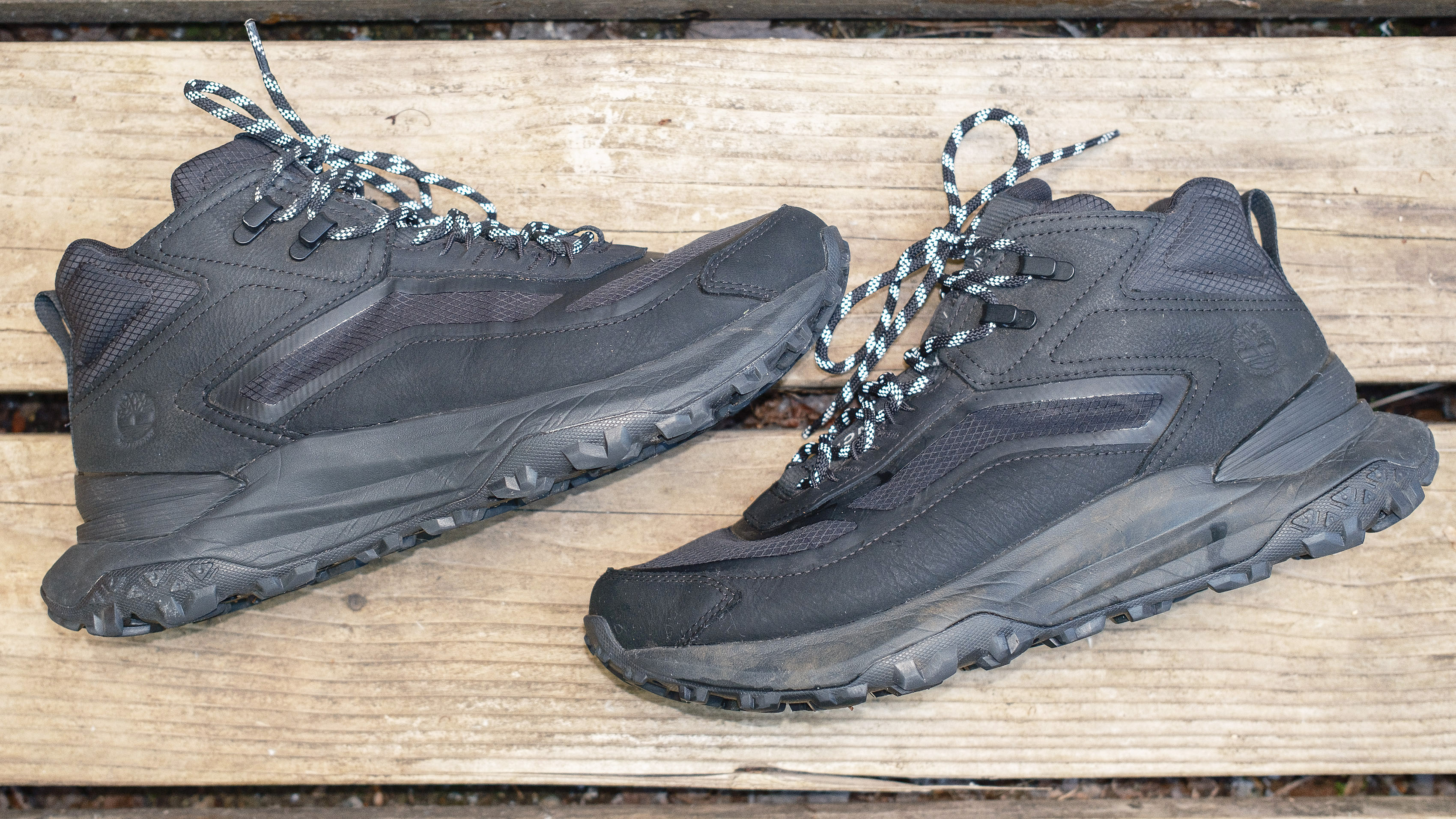 Close-up of the side of the Timberland Motion Access Mid Waterproof Sneakers (shown in black) on a wood deck