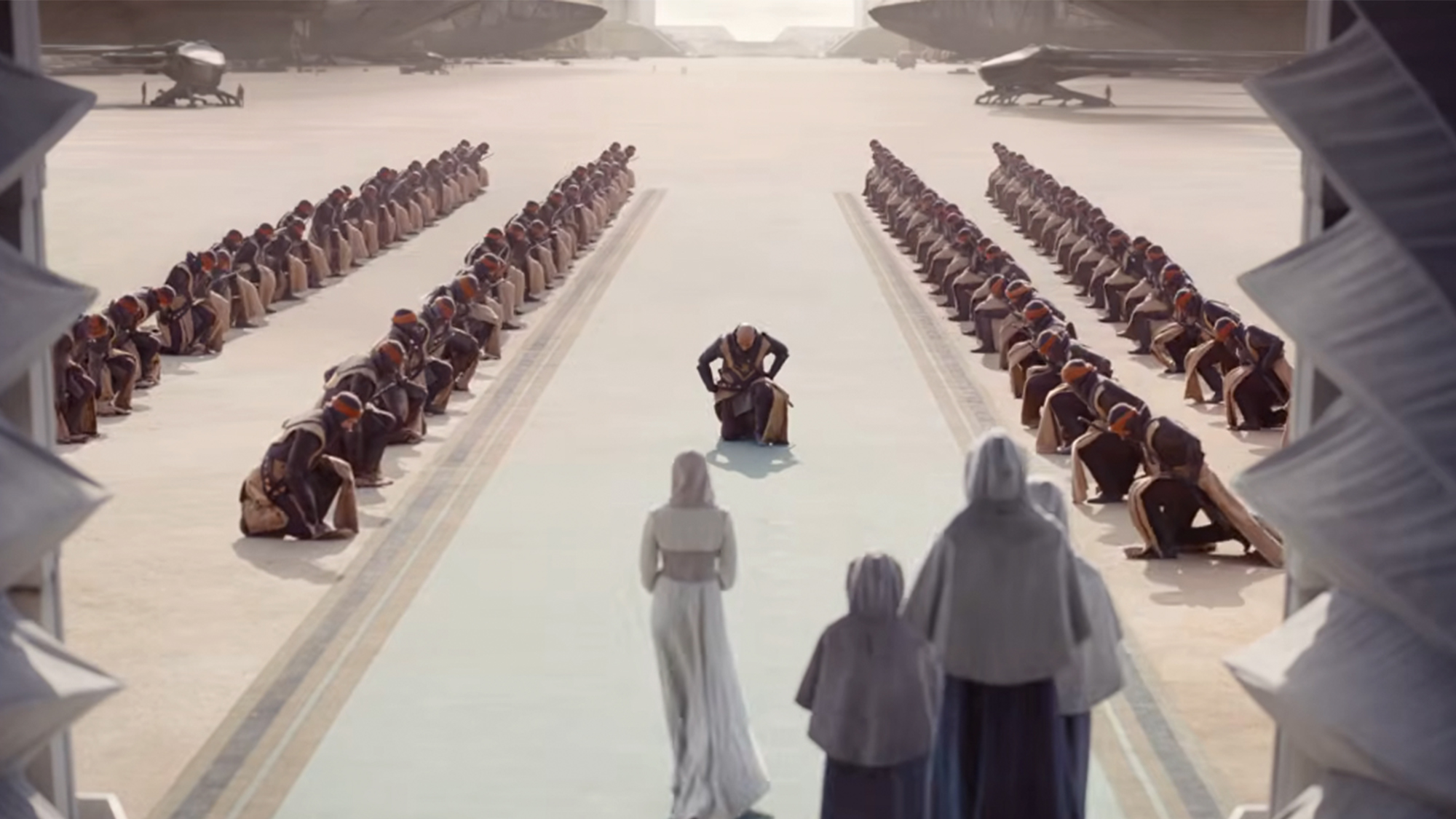 A person in all white, covered in a veil walking between rows of people bowing in Dune Part 3