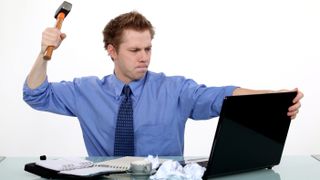 An angry office worker preparing to smash his laptop with a hammer.