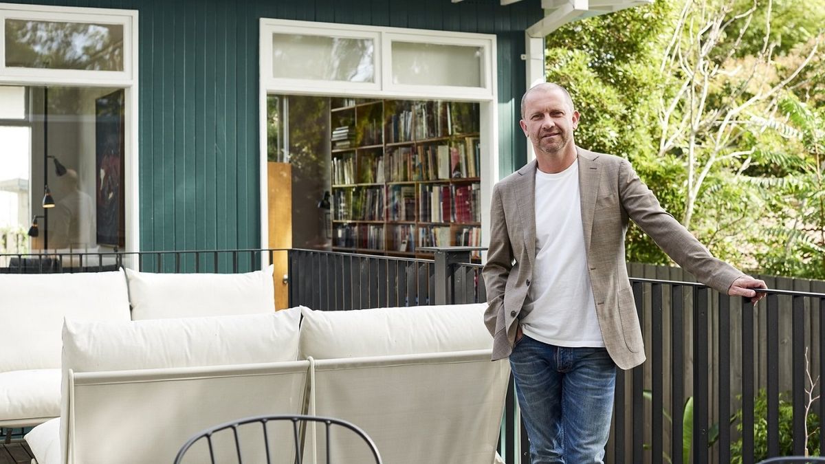 A picture of new Grand Designs Australia host Anthony Burke outside on the balcony of a sun-dappled house