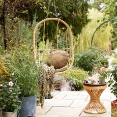a wicker hanging chair on a raised patio with a wicker table beside it and plenty of planters