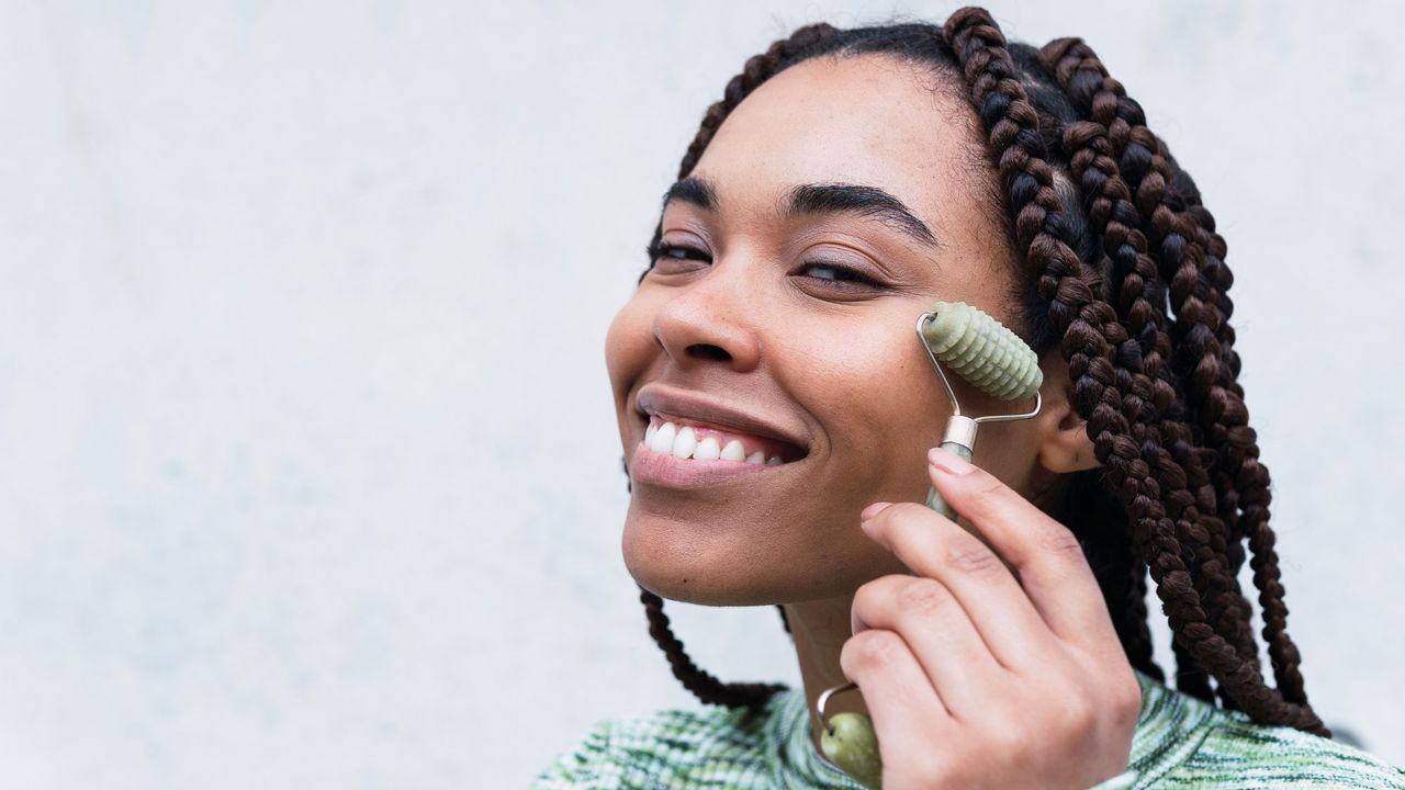 a woman using a face roller - facial massage