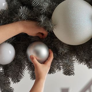 Close up of Christmas garland with hands adding medium silver baubles to the display