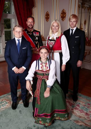 Princess Ingrid Alexandra sitting in a chair wearing a national costume posing with Prince Sverre Magnus, Crown Prince Haakon, Crown Princess Mette-Marit and Marius Borg Hoiby standing behind her during her confirmation