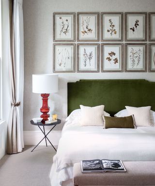 Master bedroom with bed with velvet green headboard, white bed linen, eight frames of pressed flowers above bed, bedside table with red table lamp