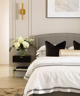 A modern guest bedroom with gray walls, a gray bed with white bedding and black pillows, and a nightstand with white flowers