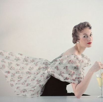 a woman modelling womens fashions in a studio portrait, wearing a white floral print shawl over a black dress while posing with a wine glass, circa 1960 the shawl is extended out behind the model photo by archive photosgetty images