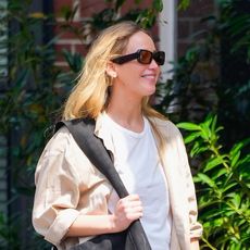 Jennifer Lawrence wearing a white tee, beige button-down, butter yellow parachute pants, and maxi black tote bag while out in New York City June 2024