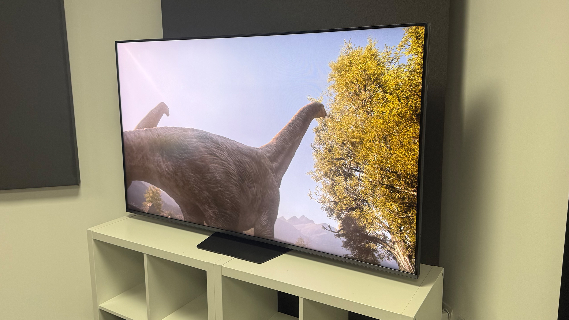 The 65-inch Hisense UR9 RGB Mini LED TV, photographed on a white, wooden unit. On the screen is a still from Netflix documentary, The Dinosaurs.