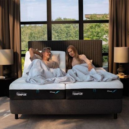 A man and woman sat together on 2 single TEMPUR mattresses on a 1 double bed frame in front of a large window