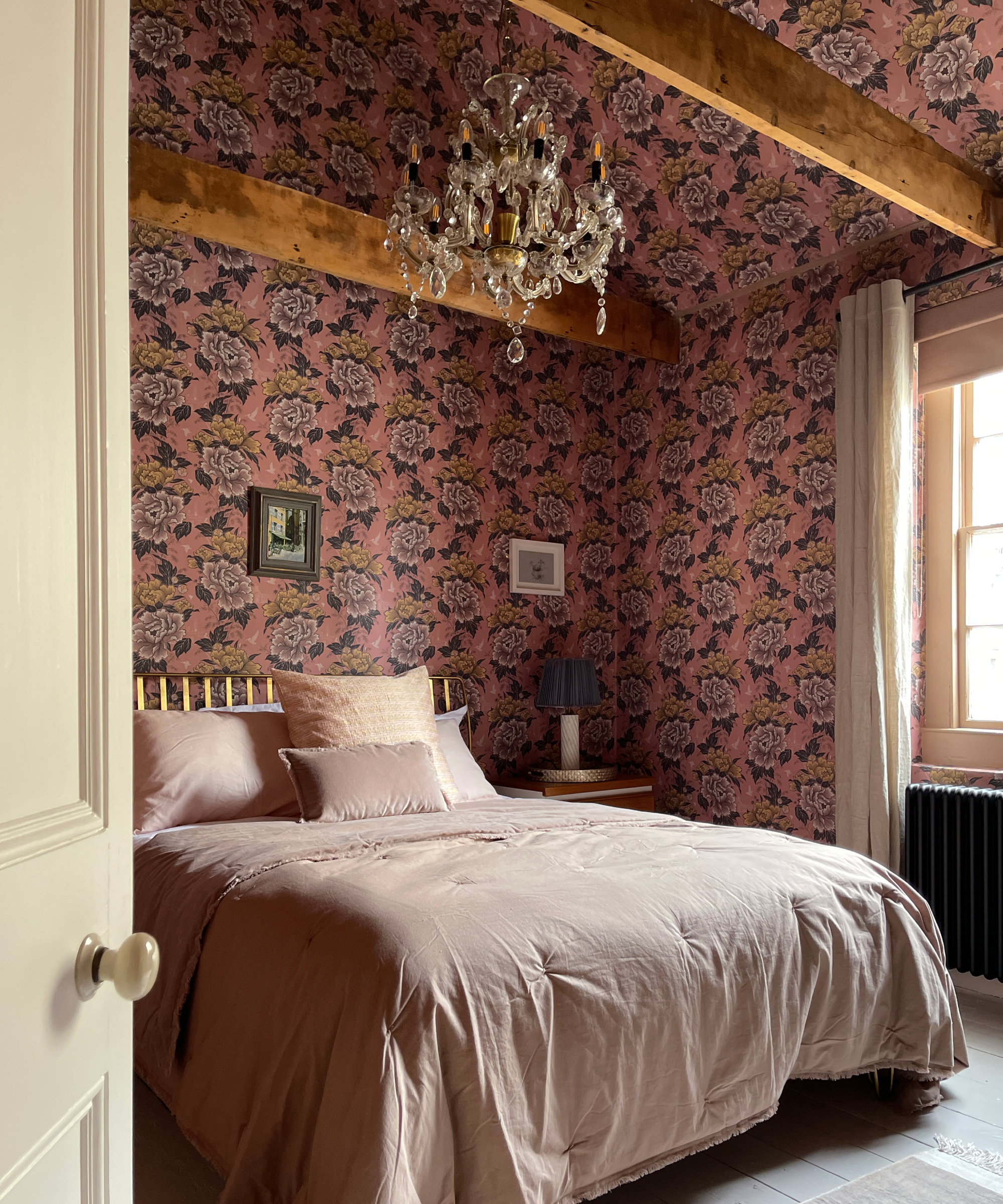 bedroom with pink floral wallpaper on walls and ceiling in between wooden beams