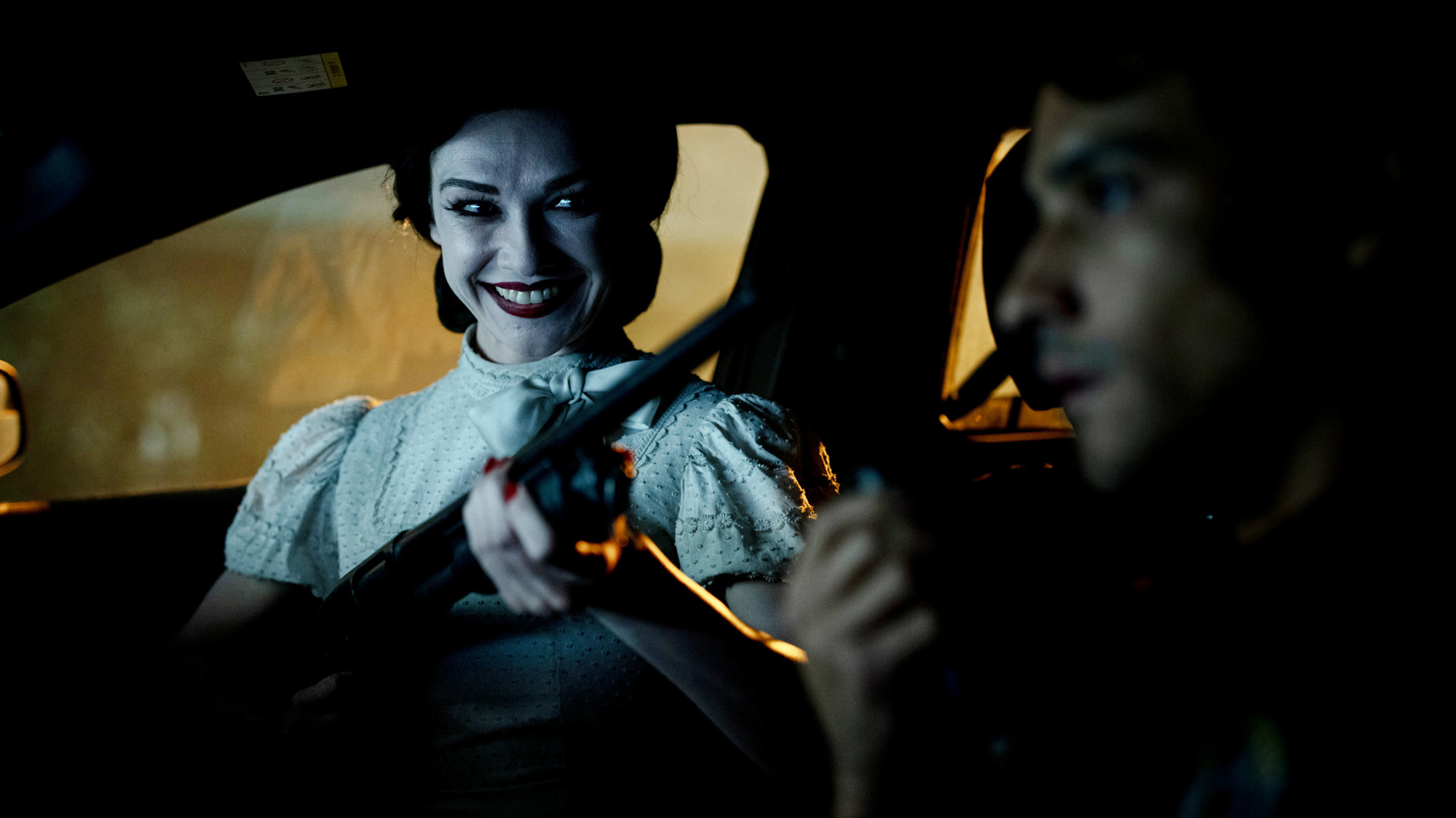 A demonic woman wearing a terrifying smile as she looks at someone in a car in Insidious: Out of the Further