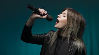 Woman in leather jacket sings into a microphone