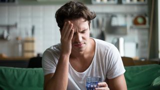 Man holding glass of water and rubbing his forehead