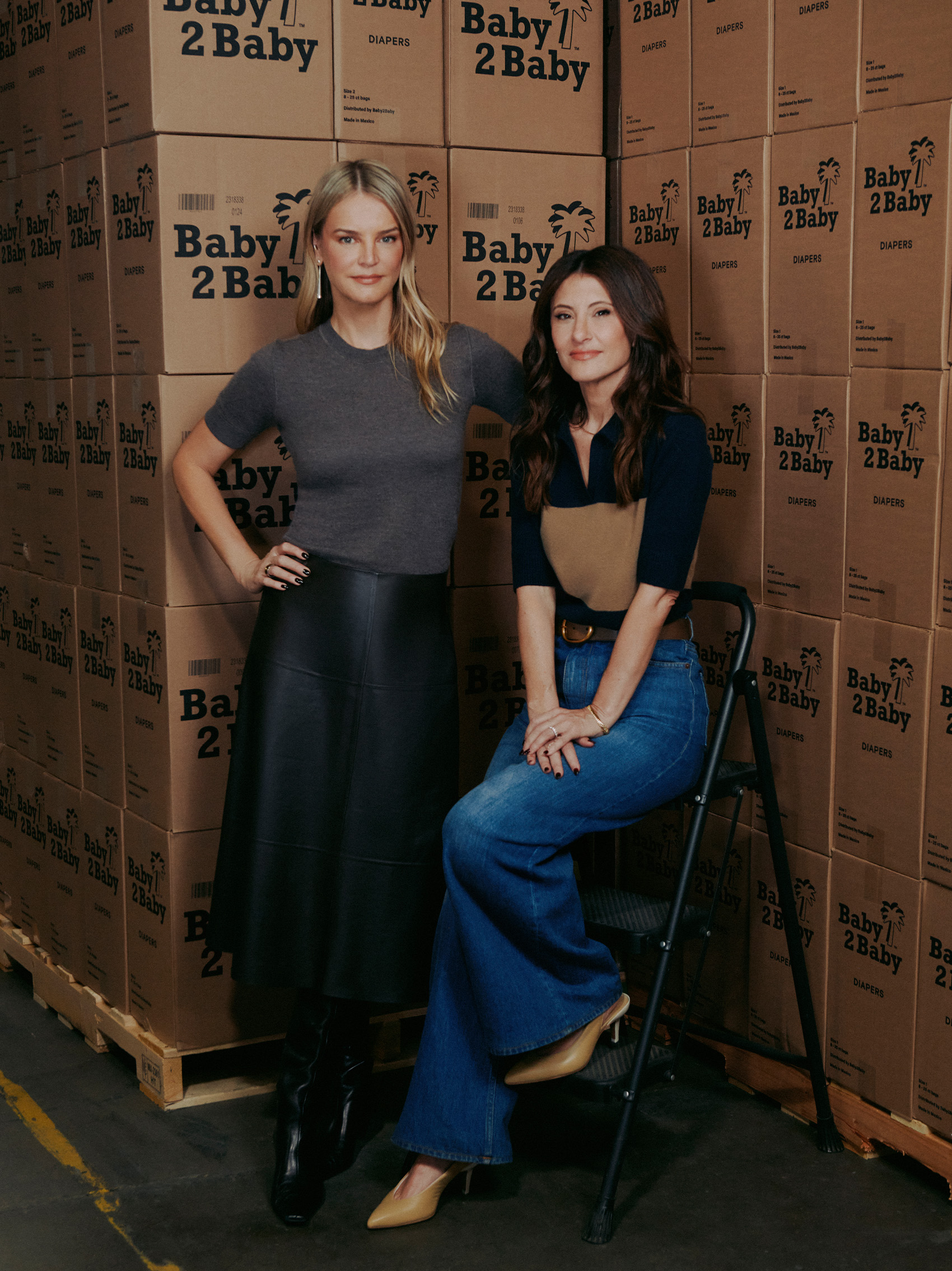 A portrait of Baby2Baby co-CEOs Kelly Sawyer Patricof (L) and Norah Weinstein (R) in front of cardboard boxes.
