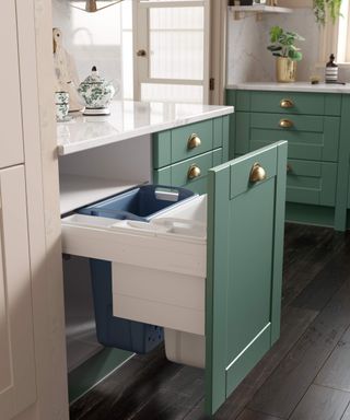 Modern green shaker kitchen cabinetry with brass handles and blue and white kitchen trash cans inside