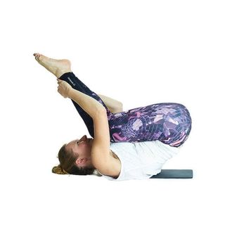 Woman in exercise clothes rolling feet up towards her head into a ball, toes pointing to the ceiling