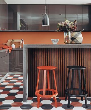 Breakfast bar in kitchen with coloured floor tiles, black units and terracotta walls.
