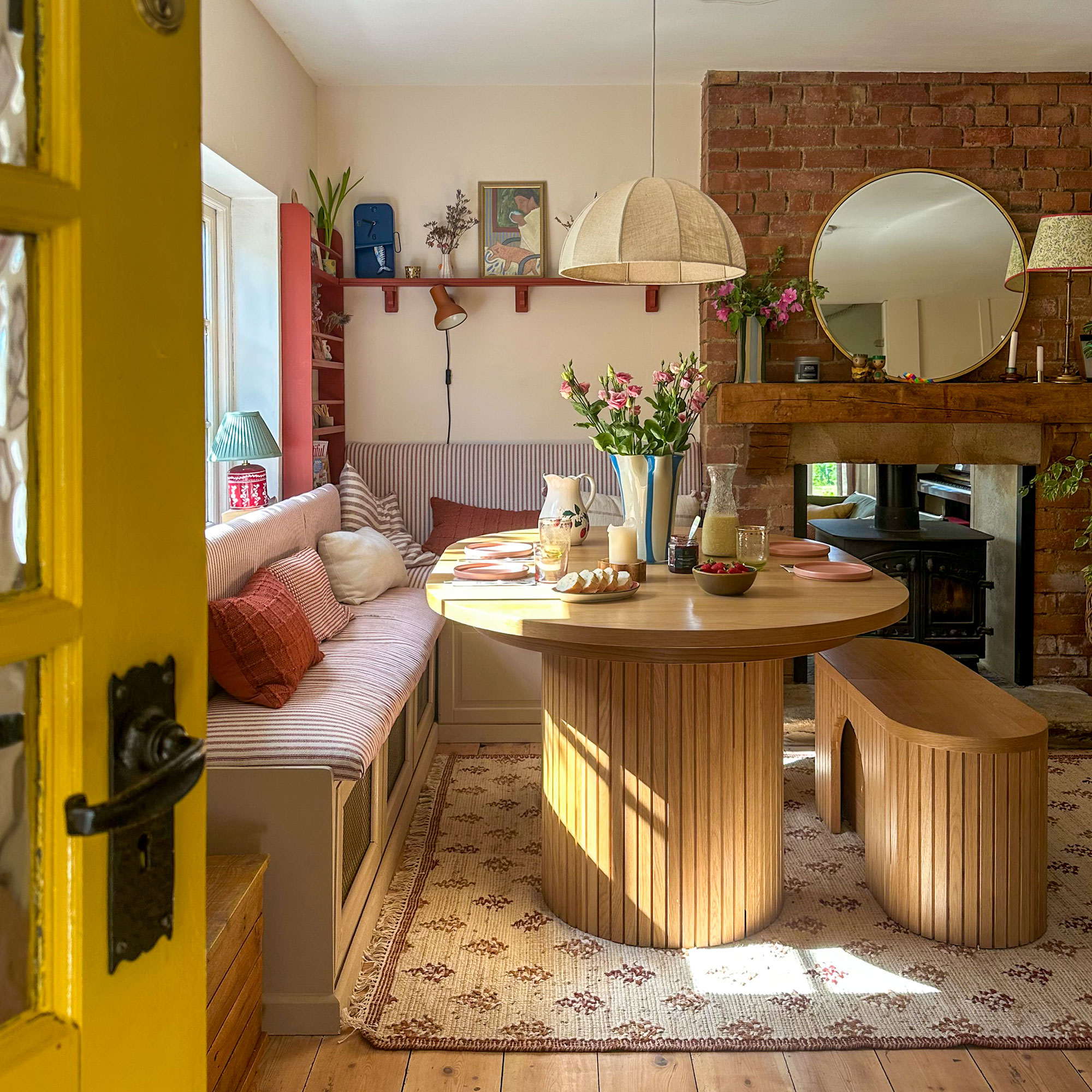Dining area with upholstered banquette around wooden table and bench on patterned rug, topped with pendant light shade
