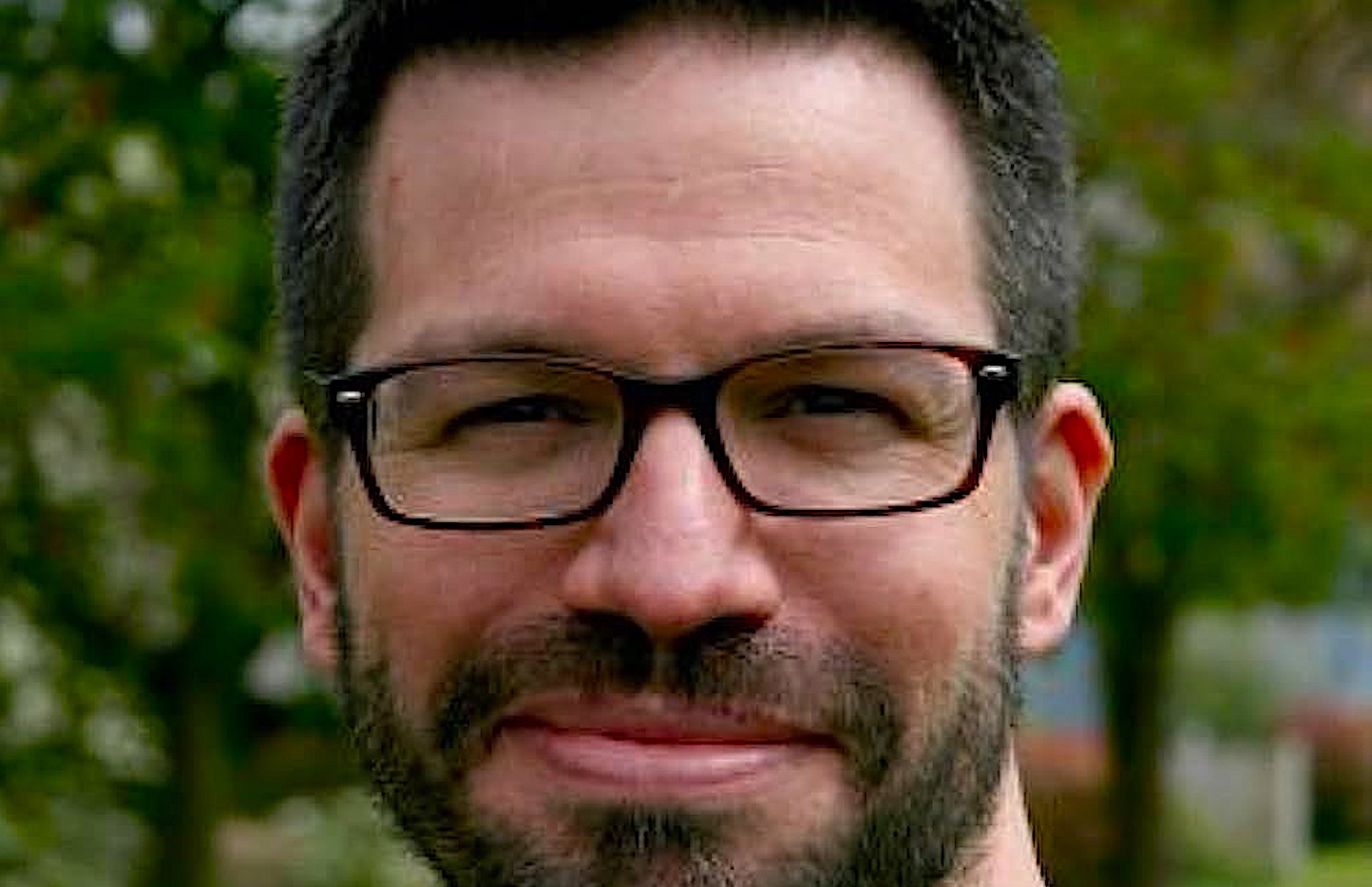 a bearded man with black-framed glasses