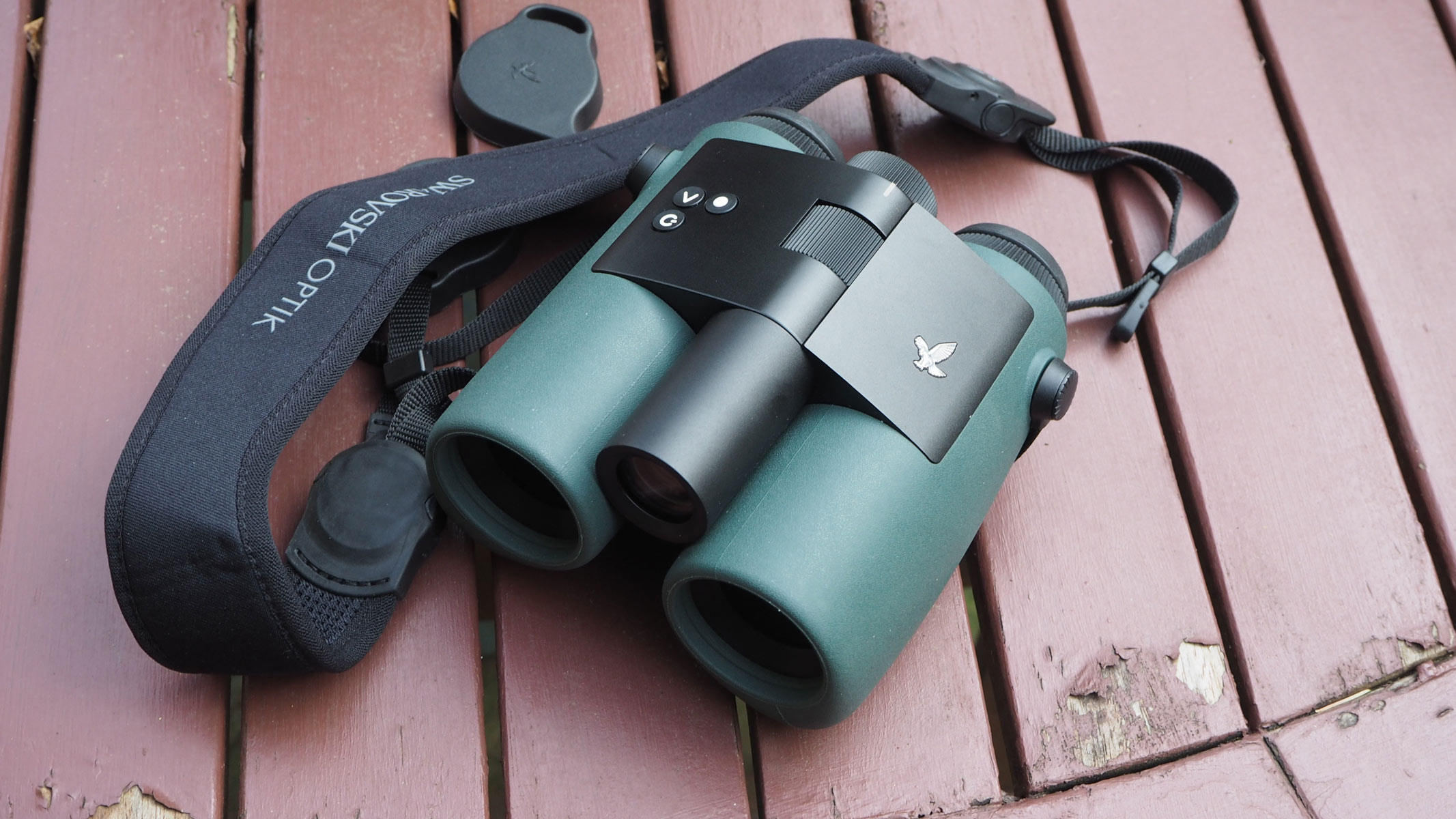 Swarovski AX Visio binocular with neck strap on a wooden slatted table.