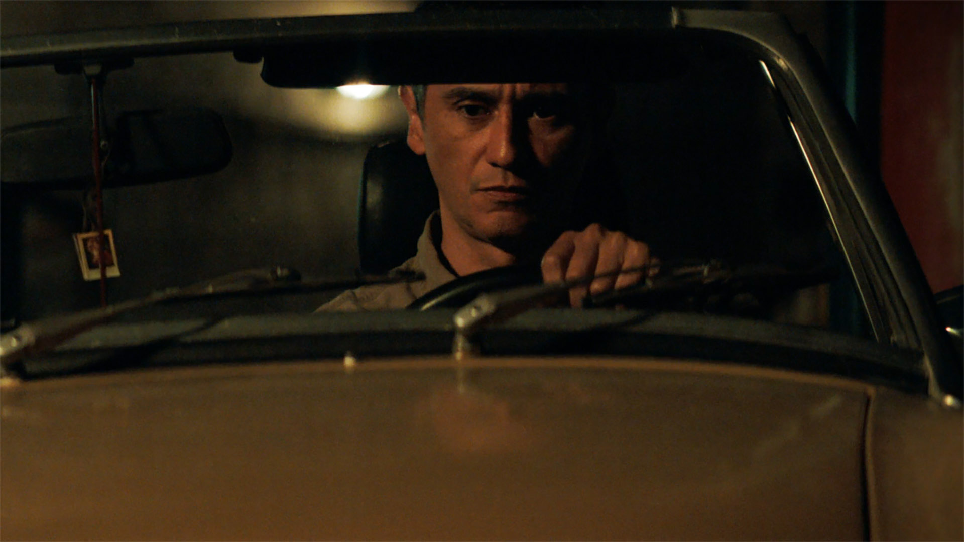 Manousos sitting in his top-down car at night in Pluribus episode 5