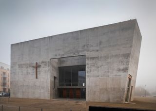 Maria Magdalena Church / Double Church For Two Faiths by KSG Architekten. A large concrete structure with a large doorway in the middle and an angled right hand side of the building.