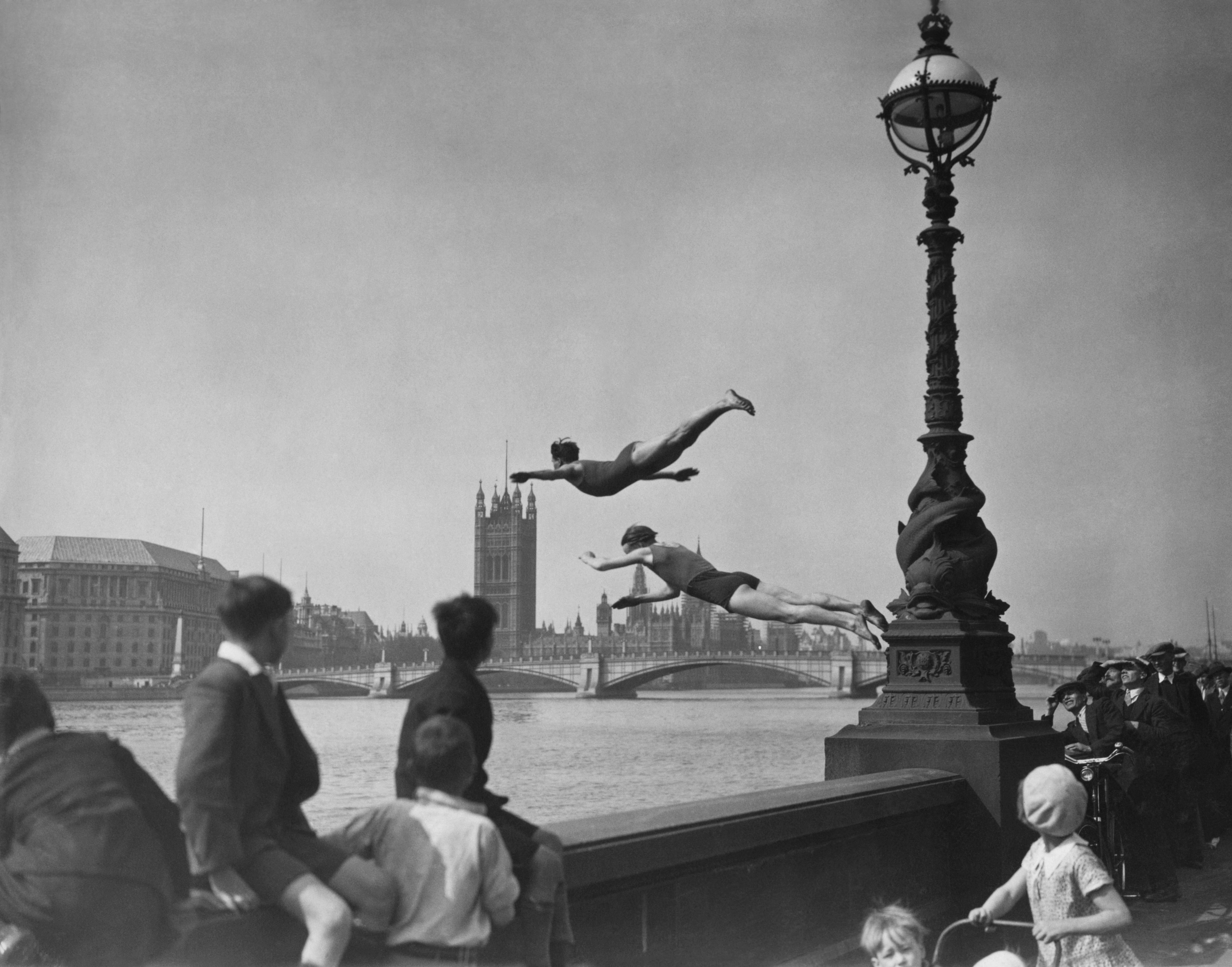 Two boys dive into the River Thames while a group of children look on