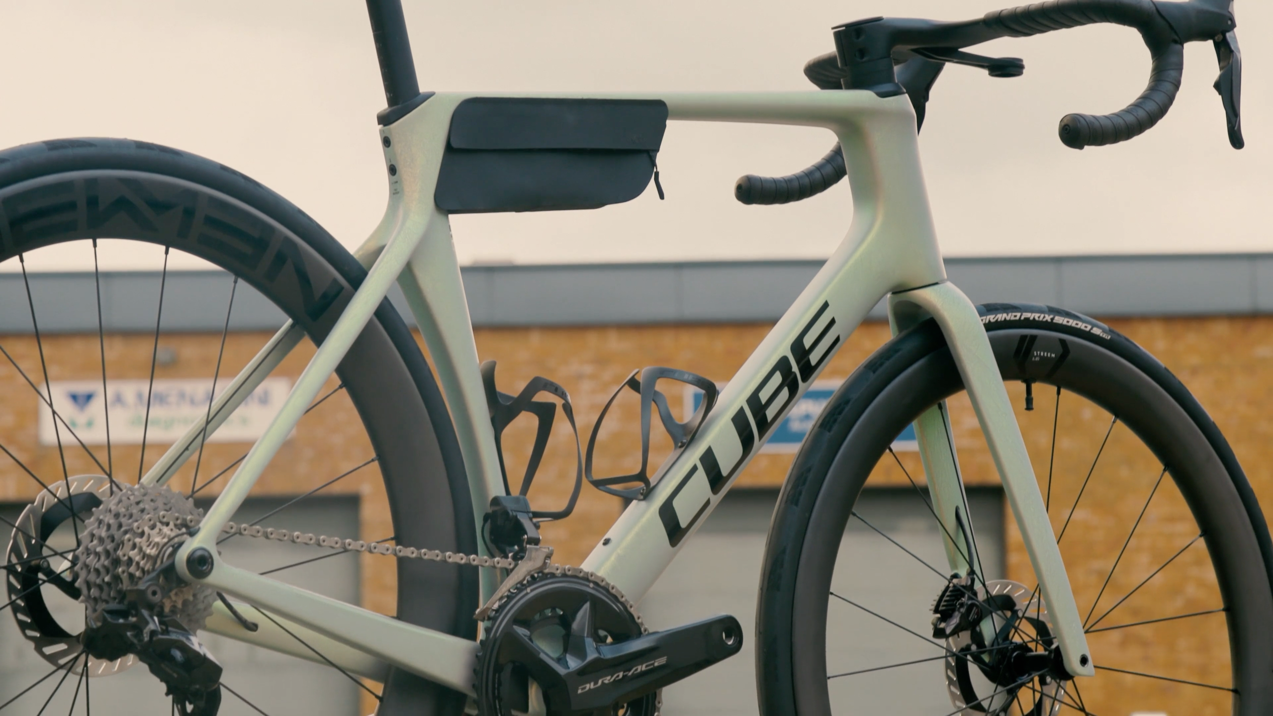 A silver Cube aero road bike in an urban environment with black carbon wheels and a bag
