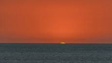 A photograph of a sunset over the ocean with a green flash around the sun.