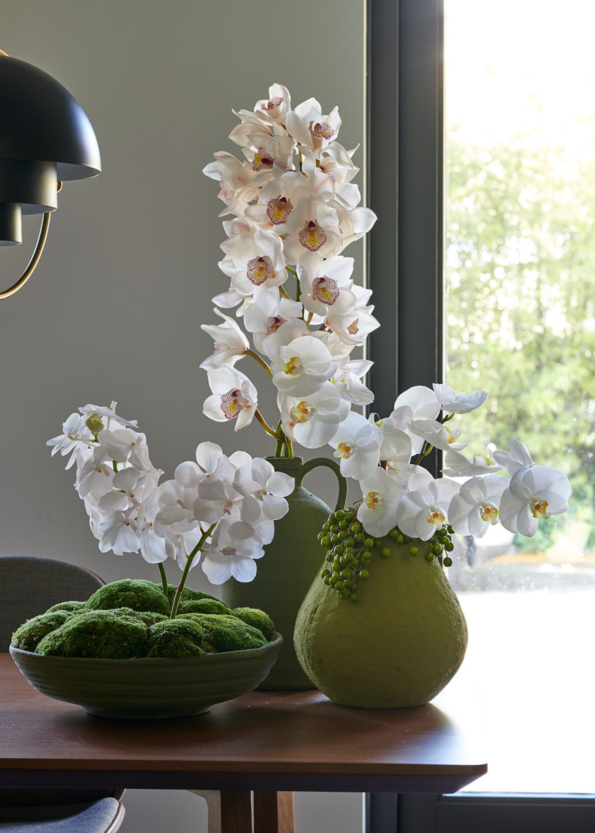 A moss planter with white orchids and a green jug with white orchids in bloom