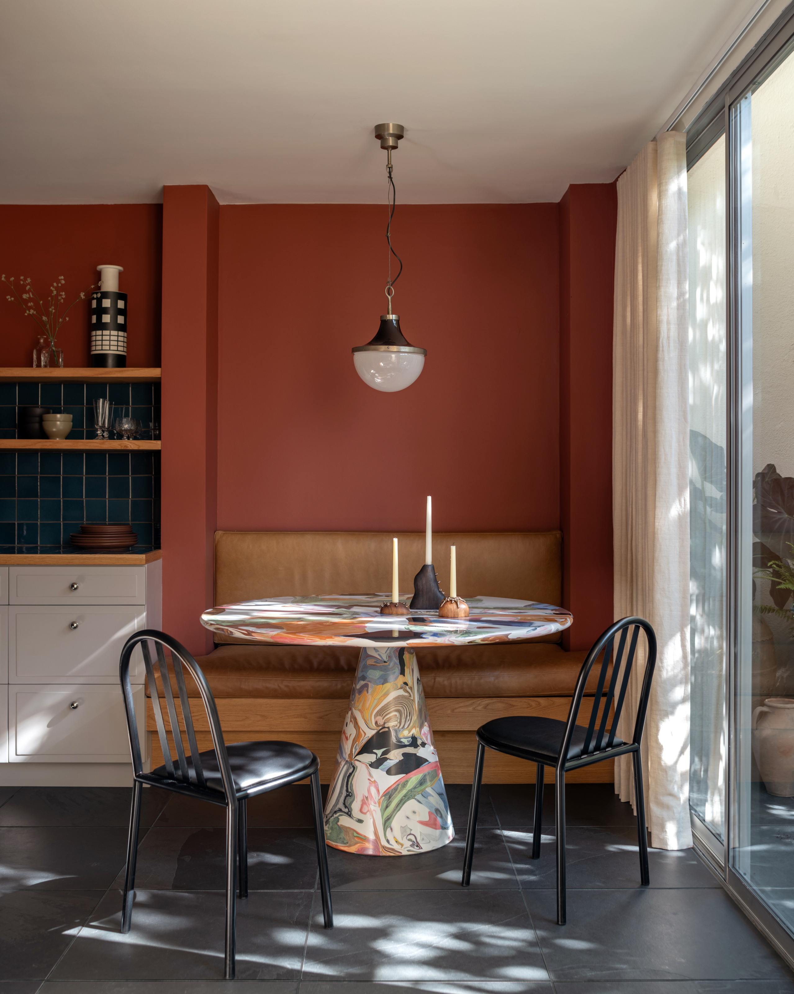 Terracotta painted breakfast nook with tan leather built-in banquette, multicolour round pedestal table and black chairs
